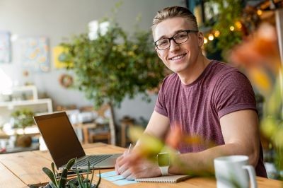 Side-view-shot-of-young-man-looking-at-camera-and-smiling-while-sitting-on-working-place-in-creative-office
